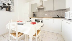 Una cocina compacta con muebles blancos, un microondas, una estufa y una mesa de comedor para cuatro personas.