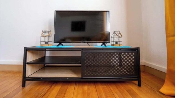 Un mueble bajo negro para televisor con un televisor de pantalla plana, dos portavelas de vidrio y un tapete azul.