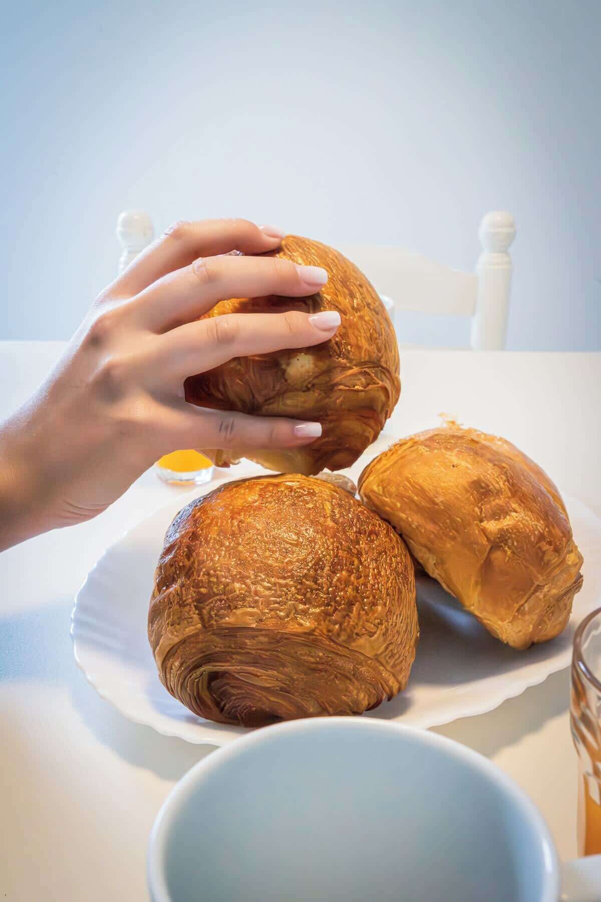 Una mano che tiene un cornetto, con altri due su un piatto e un bicchiere di succo d'arancia sullo sfondo.