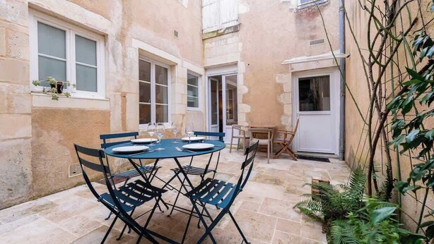 A courtyard with a round table and chairs, surrounded by stone walls and windows. - Appartement de l'ammonite (La Rochelle)
