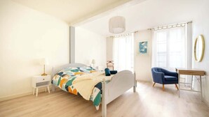 A bedroom with a bed, bedside table, chair, and a desk. - Appartement de l'ammonite (La Rochelle)