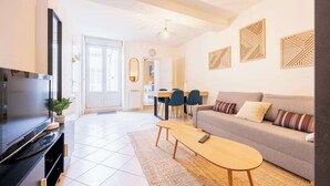 A modern living room with a flat-screen TV, a sofa, a coffee table, and a dining area with chairs and a table. - Appartement de l'ammonite (La Rochelle)