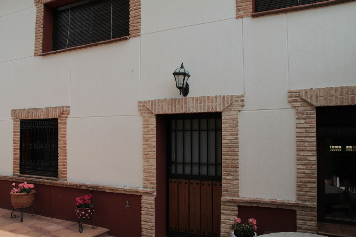 A building with a white facade, brick accents, a wooden door, and a window with a metal grill.
