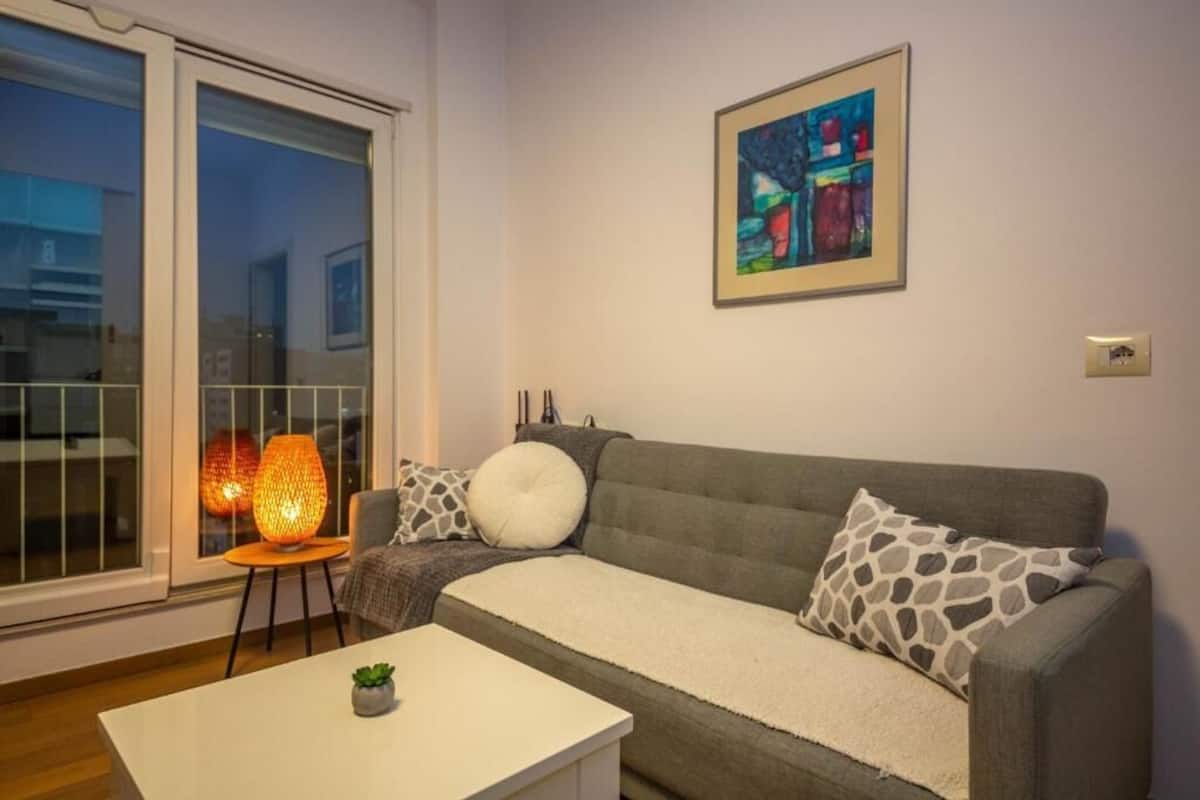 Una sala de estar con un sofá, una mesa de centro, una lámpara de pie y un cuadro en la pared.