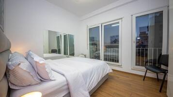 Un dormitorio moderno con una cama grande, una silla y un balcón con puertas de vidrio.