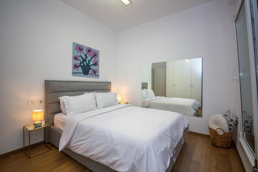 A bedroom with a bed, bedside tables, a lamp, a wall-mounted mirror, and a painting.