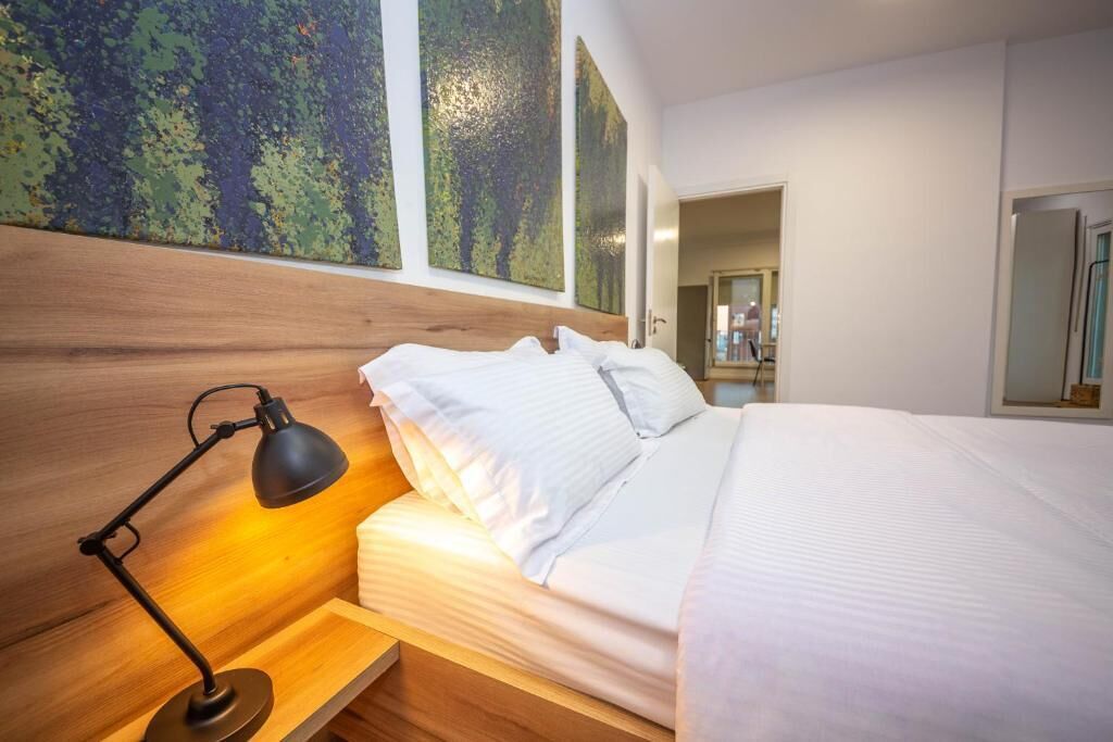 Un dormitorio moderno con cabecera de madera, lámpara de noche, cama bien hecha y grandes cuadros abstractos en la pared.
