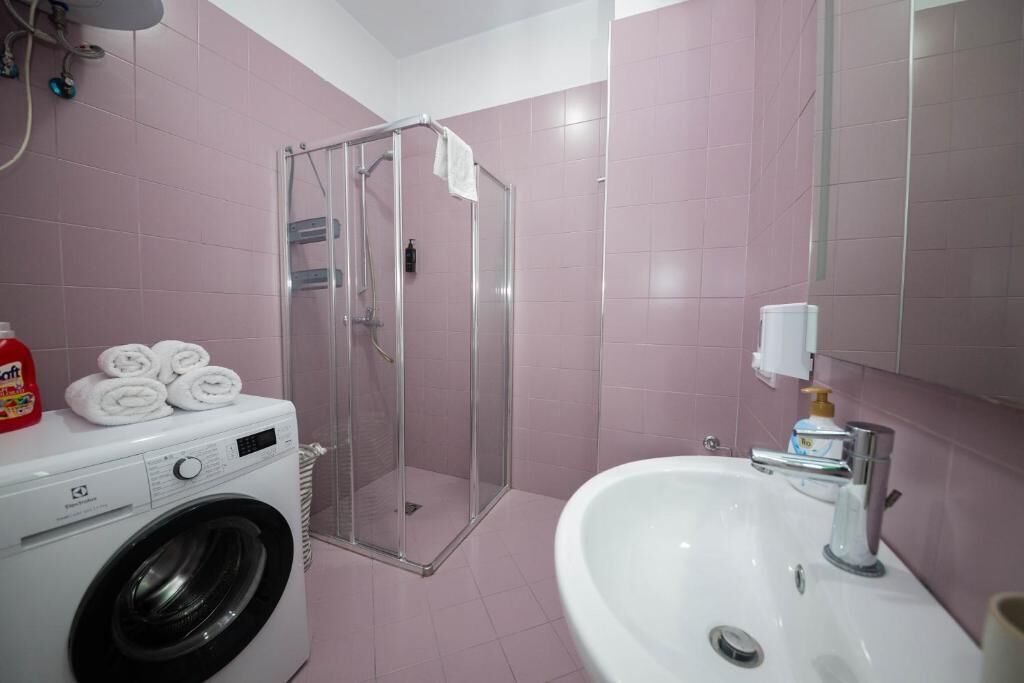 A bathroom with a washing machine, a glass shower enclosure, and a sink with a mirror.