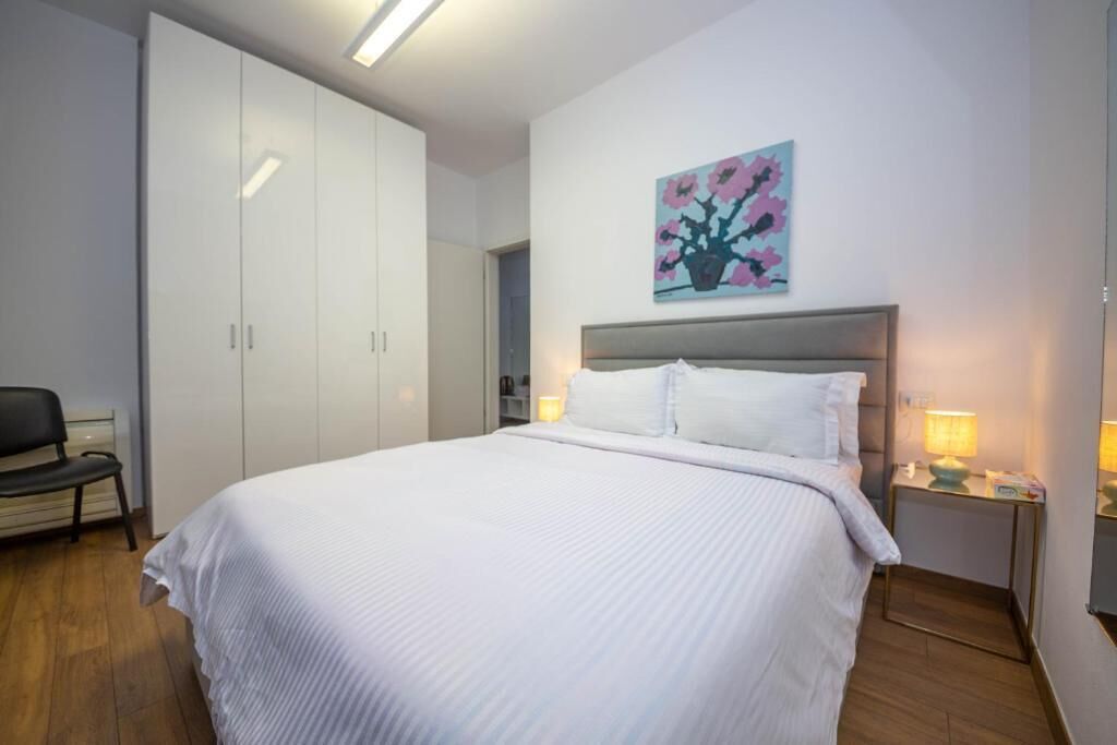 Une chambre à coucher comprenant un lit, une chaise, une armoire et une table de chevet avec une lampe.