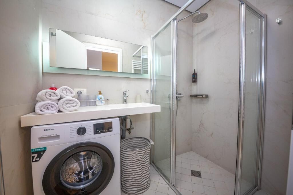 Un bany modern amb rentadora, plat de dutxa de vidre i mirall sobre el lavabo.