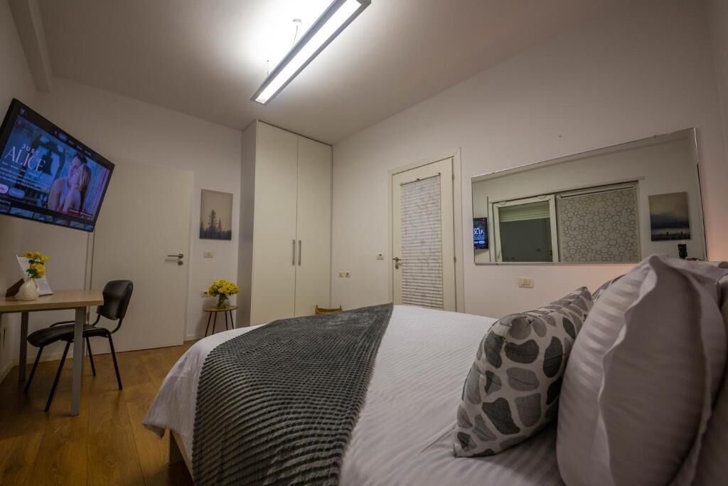 Une chambre à coucher comprenant un lit, un bureau, une chaise, un téléviseur et une fenêtre avec des stores.