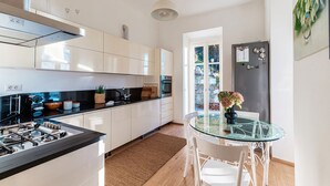A modern kitchen with white cabinets, a black countertop, a glass table, and white chairs. - Villa Rocawood (Brunate)