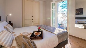 A bedroom with a bed, a bedside table with a lamp, a window with a view of trees, and a door leading to a balcony. - Villa Rocawood (Brunate)