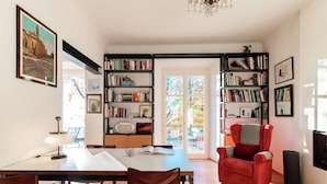 A spacious living room with a dining area, a red armchair, and a bookshelf filled with books. - Villa Rocawood (Brunate)