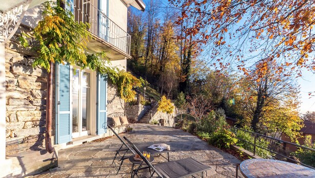 A stone patio with outdoor furniture, a stone wall, and a building with blue shutters. - Villa Rocawood (Brunate)