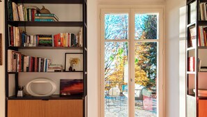 A room with a large bookshelf filled with books, a white circular object on a wooden cabinet, and a glass door leading outside. - Villa Rocawood (Brunate)