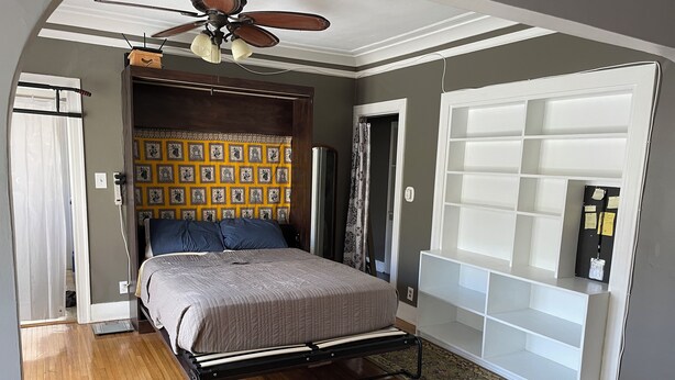 Een slaapkamer met een bed, een plafondventilator, een behang, een kledingkast en een vloerkleed.