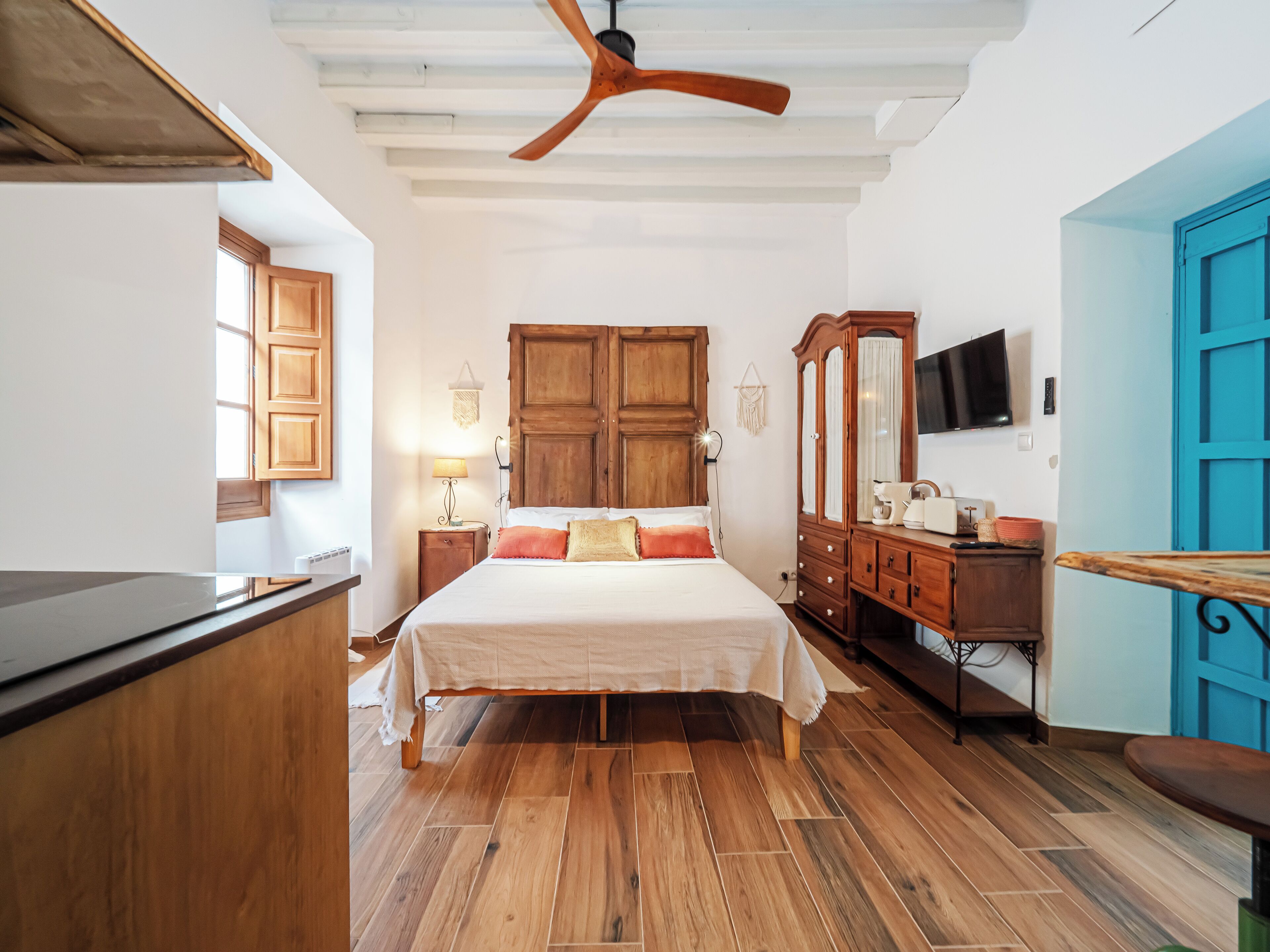 Un dormitorio con una cama de madera, un ventilador de techo, un armario y un televisor en la pared.