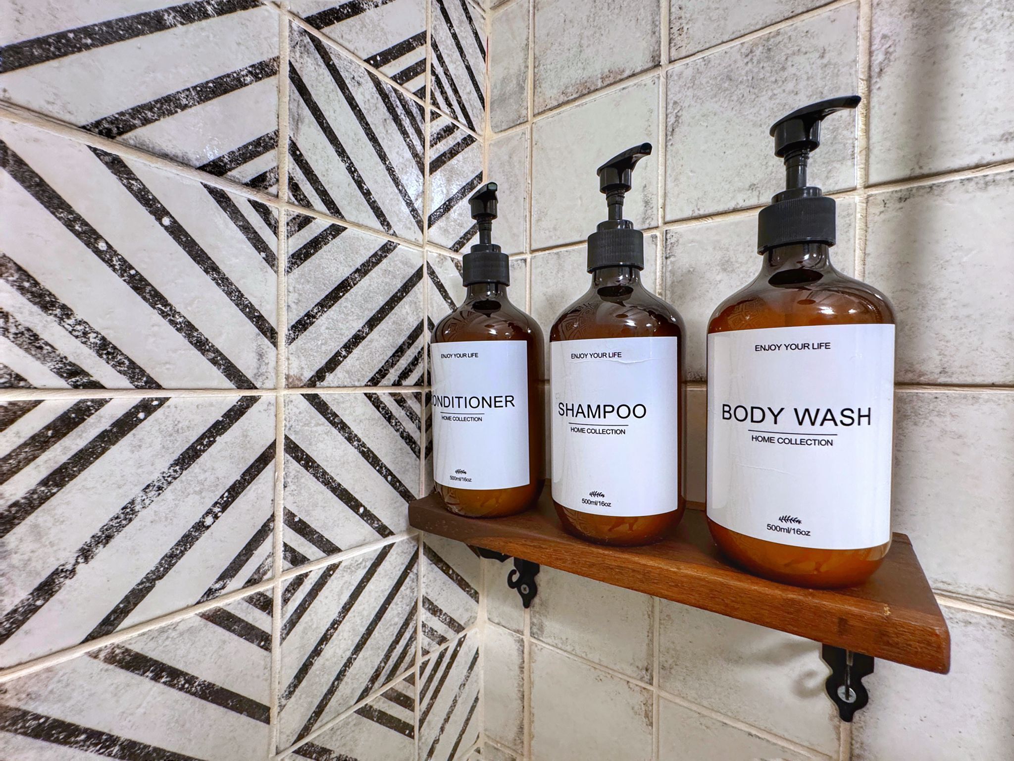 Three bottles of personal care products on a wooden shelf against a tiled wall.