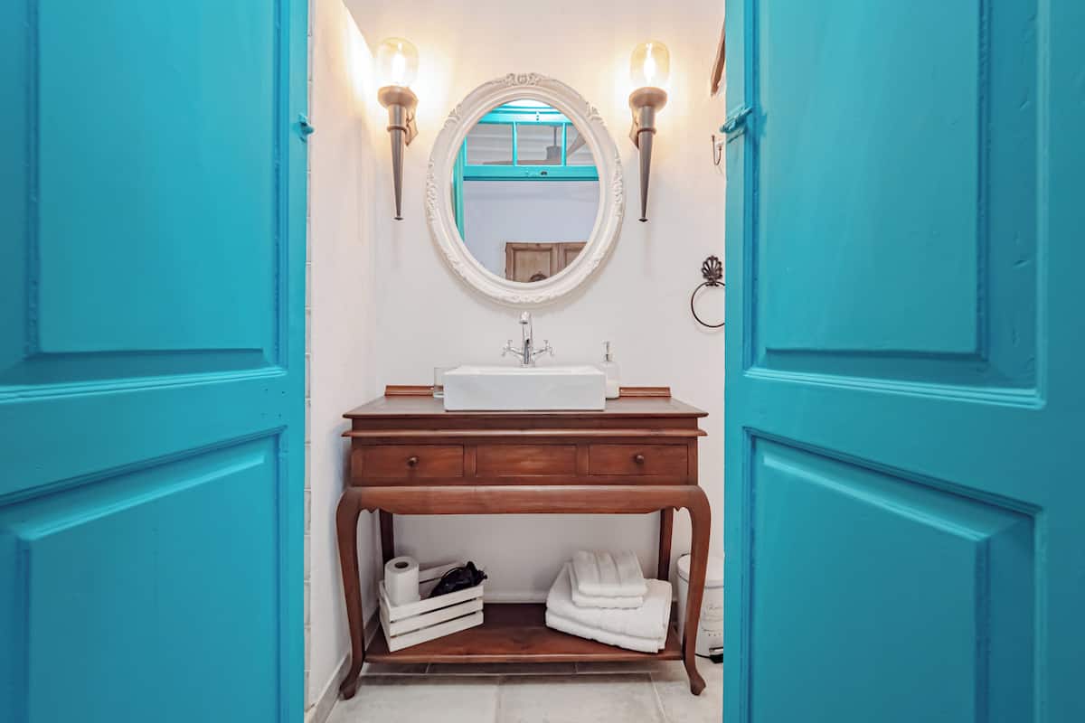 A bathroom with a wooden vanity, white sink, and a mirror above it. There are two wall-mounted lights and a towel rack.