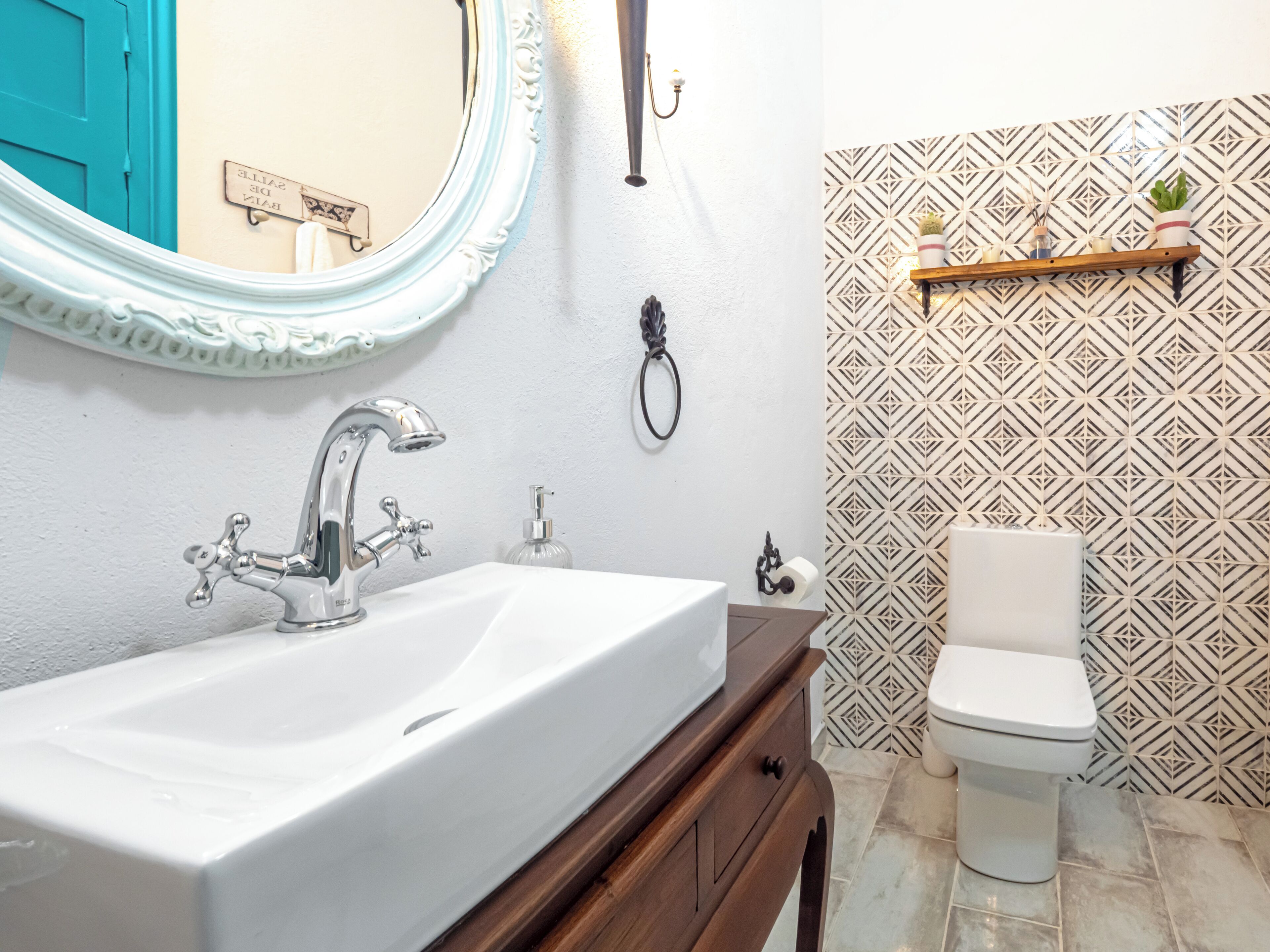 Ein Badezimmer mit weißem Waschbecken, einem Spiegel, einer Toilette und Wandpapier mit Muster.