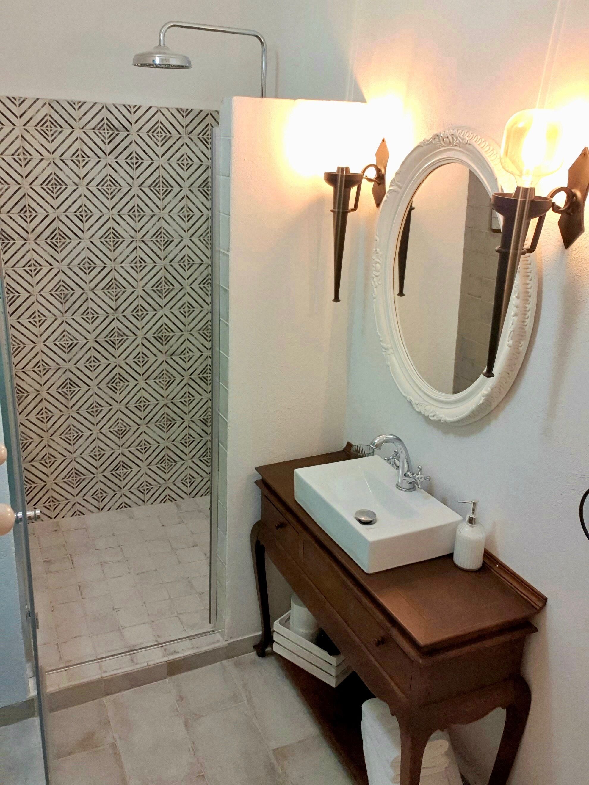 A bathroom with a shower, a sink with a mirror, and a patterned wall.