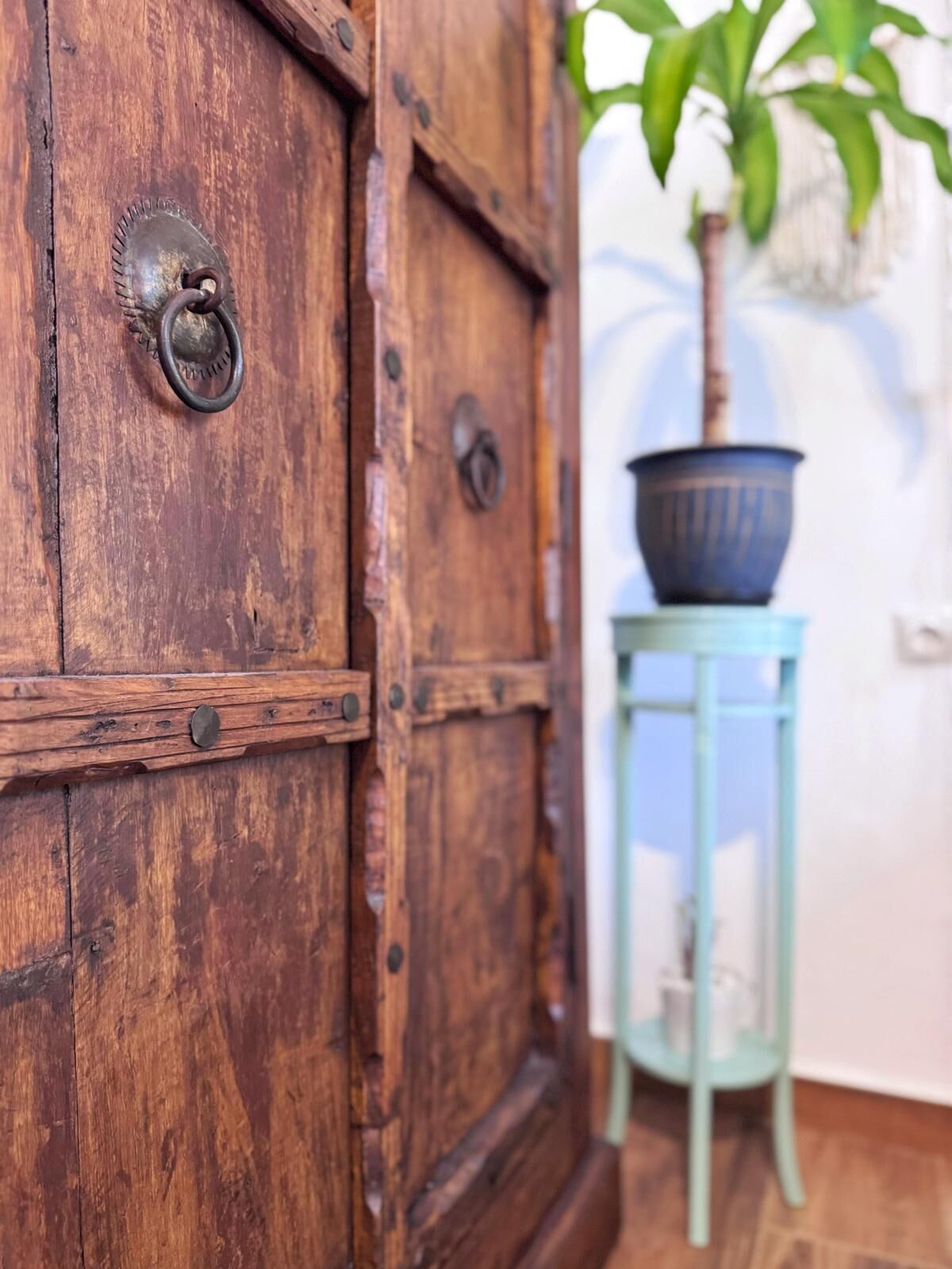 A wooden cabinet with a metal handle and a small table with a potted plant beside it.