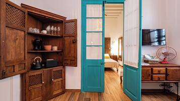 A room with wooden cabinets, a teal door, a bed, a TV, and a fan.