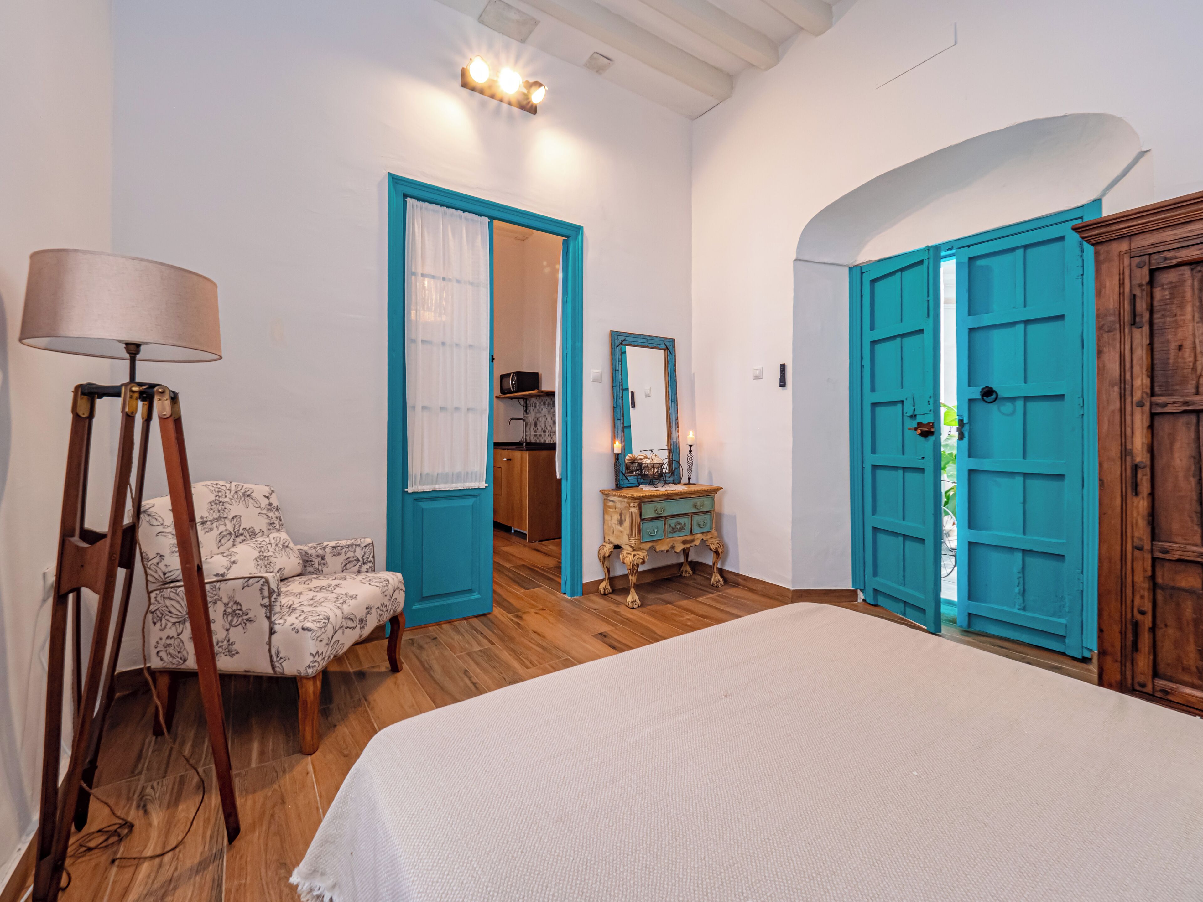 A bedroom with a bed, a lamp, a chair, a dresser, and a door.