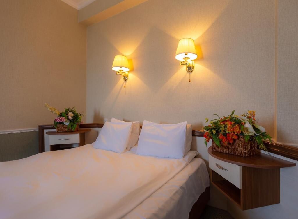A hotel room with a bed, two nightstands, and wall-mounted lamps.