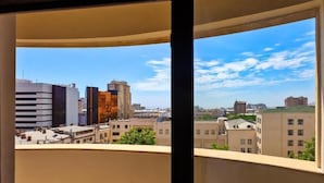 Une vue sur la ville à travers une fenêtre, avec des bâtiments modernes, un ciel dégagé et un panorama sur le centre-ville.