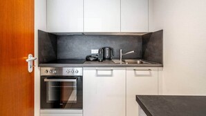 A compact kitchen with white cabinets, a black countertop, a built-in oven, and a coffee maker. - Studio 4* with balcony and parking in Bel Air (Luxembourg)