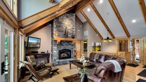 Amplia sala de estar con chimenea de piedra, muebles de cuero y vigas de madera.