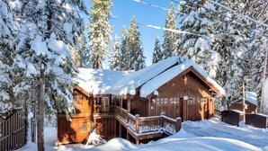 Una cabaña de madera con balcón y porche cubierto, rodeada de árboles cubiertos de nieve.