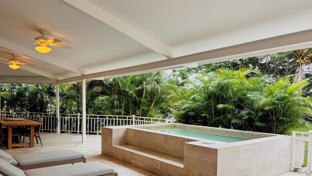 Un espacio exterior techado con piscina, sillas de descanso y una mesa.