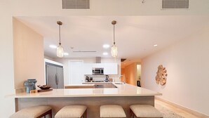 Una cocina moderna con una isla central, taburetes de bar, electrodomésticos de acero inoxidable, iluminación colgante y un elemento decorativo en la pared.