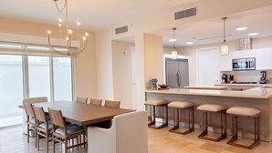 Una cocina moderna con una isla central, electrodomésticos de acero inoxidable y un comedor con una mesa grande y sillas.