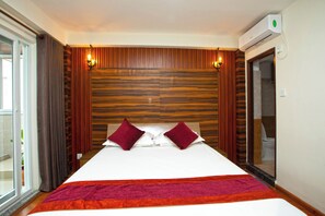 Ein Hotelzimmer mit einem großen Bett, einem Kopfteil aus Holzpaneelen, zwei roten Kissen, einer roten und orangefarbenen Bettdecke, einer Schiebetür und einem Badezimmer mit Spiegel und Toilette.