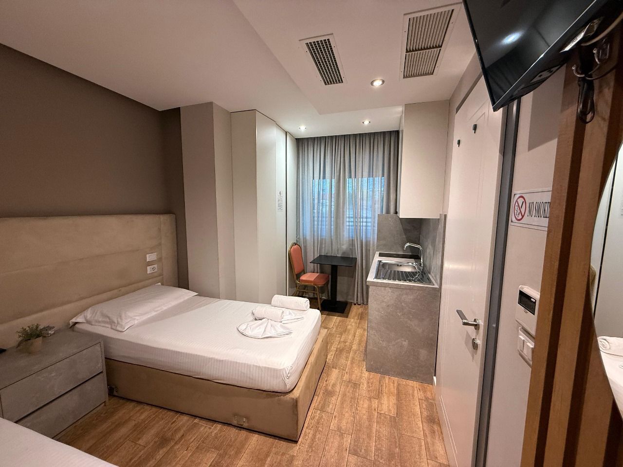 Habitación de hotel con cama, escritorio, silla, lavamanos y televisor.