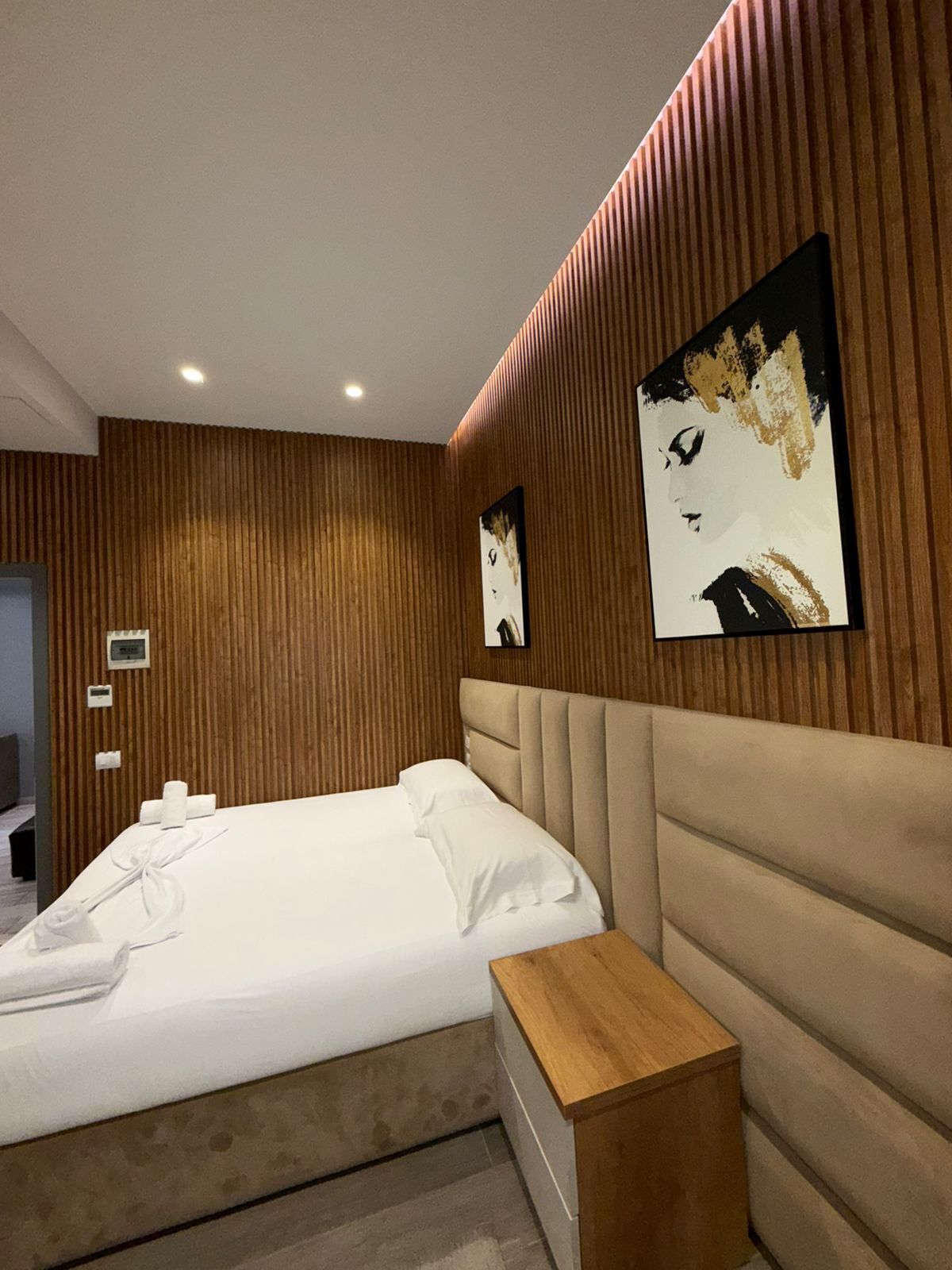 A modern hotel room with a large bed, wooden paneling on the walls, and two framed artworks.
