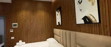 A modern hotel room with a large bed, wooden paneling on the walls, and two framed artworks.
