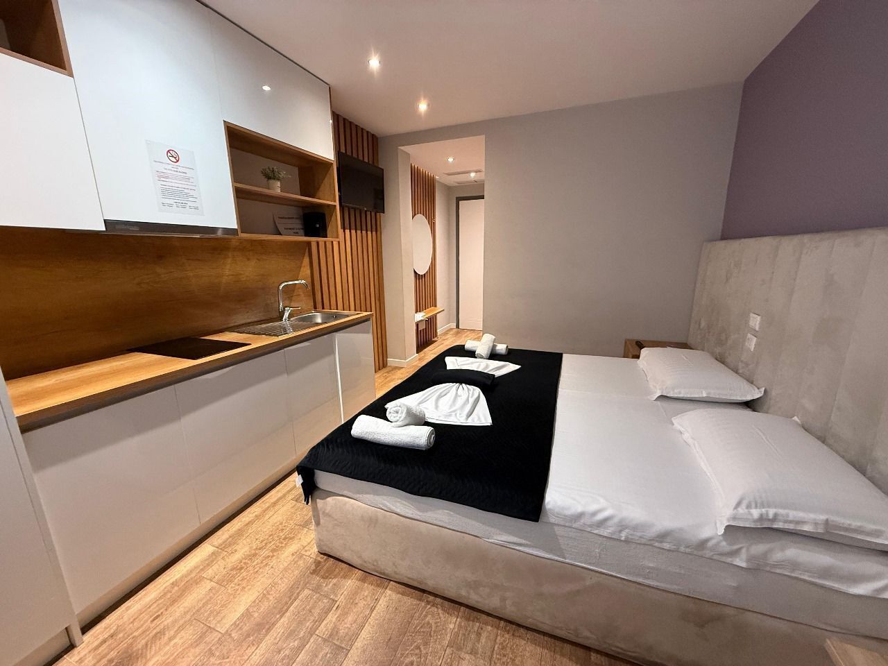 A hotel room with a bed, a wooden bench, a small table, and a mirror.