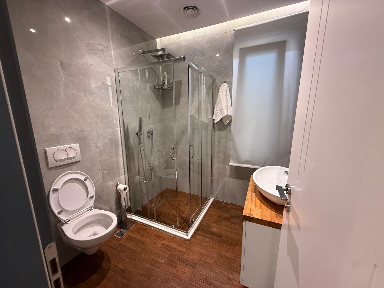 Un bagno moderno con cabina doccia in vetro, un water bianco e un lavabo con piano in legno.