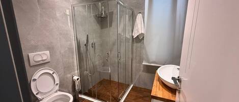 Un bagno moderno con cabina doccia in vetro, un water bianco e un lavabo con piano in legno.