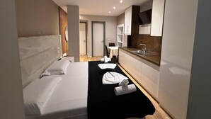 A hotel room with a bed, a small kitchenette, a bathroom, and a view of the hallway. - La Villa Bnb (Tirana)