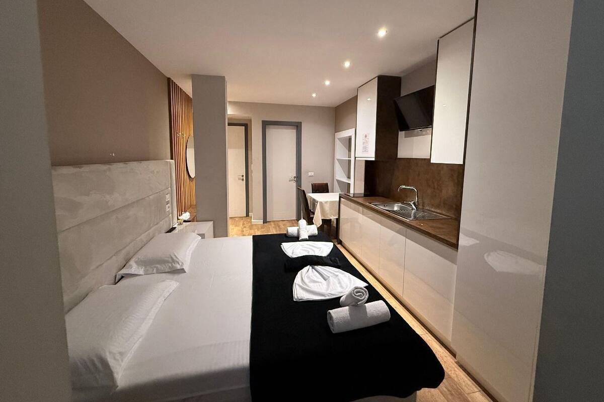 A hotel room with a bed, a small kitchenette, a bathroom, and a view of the hallway.