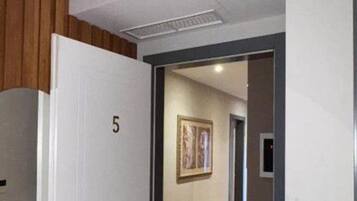Una habitación de hotel con una puerta de madera, el número 5 en la puerta, un felpudo y un pasillo con suelo de madera y un cuadro enmarcado en la pared.