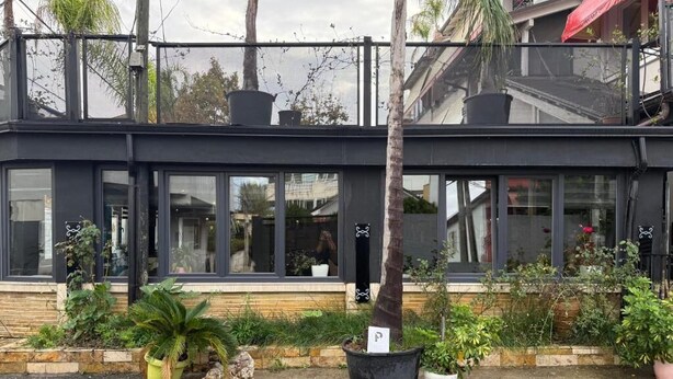 A modern building with large windows and a balcony. There are potted plants and a sign on the ground. - La Villa Bnb (Tirana)