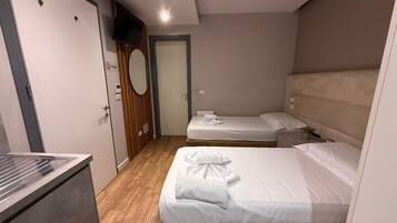 Habitación de hotel con dos camas, un televisor, suelo de madera y una puerta con letrero de 'No Fumar'.