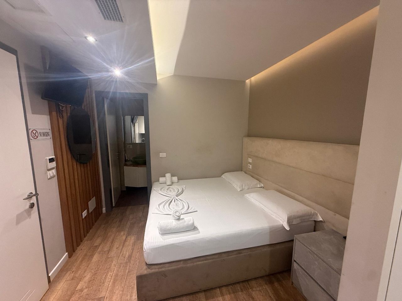 Une chambre à coucher avec un lit, des tables de chevet, un plancher en bois, une porte et un téléviseur.